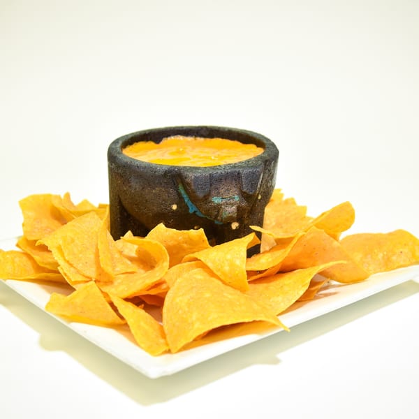 Benji's Taqueria Mexican Grill's queso dip in a molcajete, surrounded by tortilla chips on a white plate.